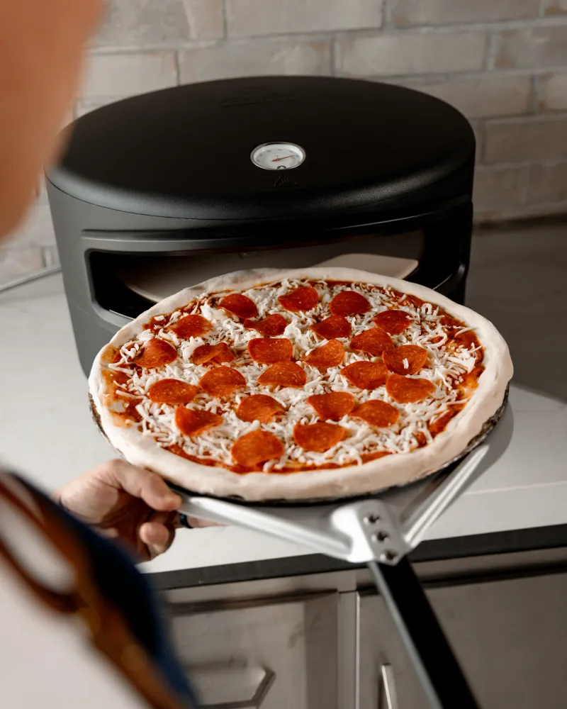 A pepperoni pizza coming off the stone