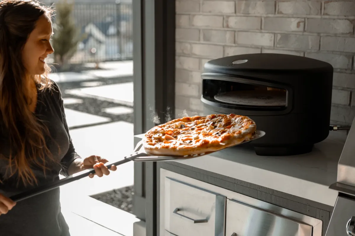 A host sliding a fresh pizza out of the Festa oven